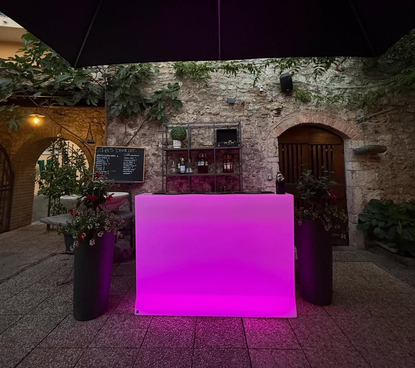 La corte la sera, con il bancone bar illuminato e il muro in pietra con l'arco